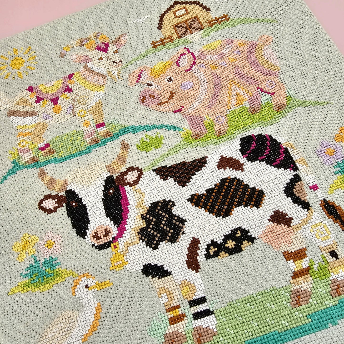 Finished Farmyard Finds cross stitch design flatlay featuring a colourful geometric cow, pig and goat on green aida fabric